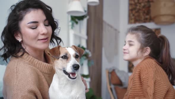 Young Mother Daughter in Knitted Sweaters are Sitting on a Bed in a Cozy Bedroom with Their Small