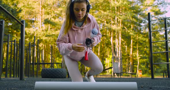 A Young Woman is Getting Ready for an Outdoor Workout She Rolls Out a Mat and Sits Down to Meditate