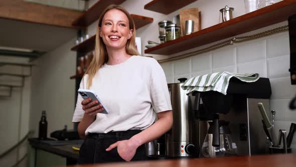 Happy blonde woman barista typing by phone