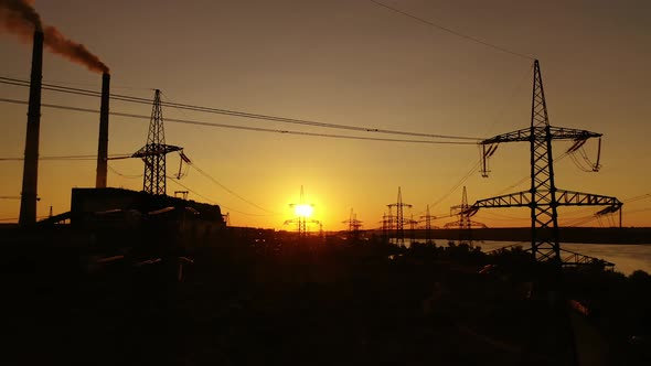 Transmission lines at sunset. High-voltage electric towers near the industrial factory