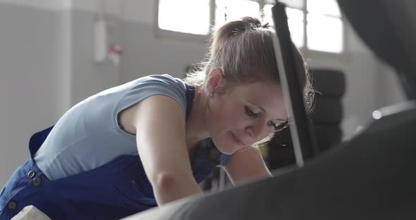 Professional female mechanic doing a car service, she is fixing the car engine