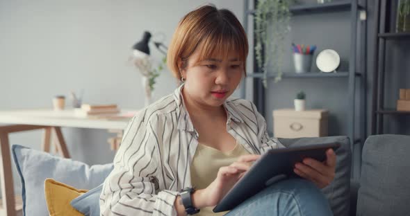 Young Asia lady using tablet text message or check social media on sofa in living room at house.