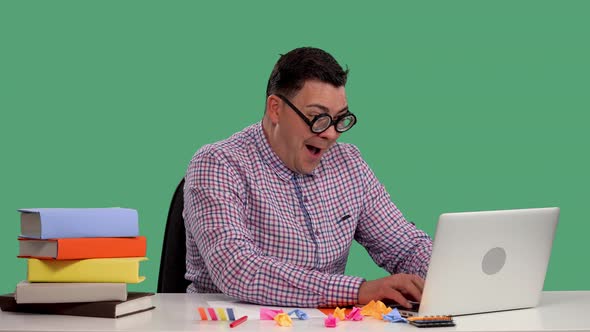 A Man Sits at a Table Uses a Laptop Enthusiastically Plays an Online Game Celebrates a Victory