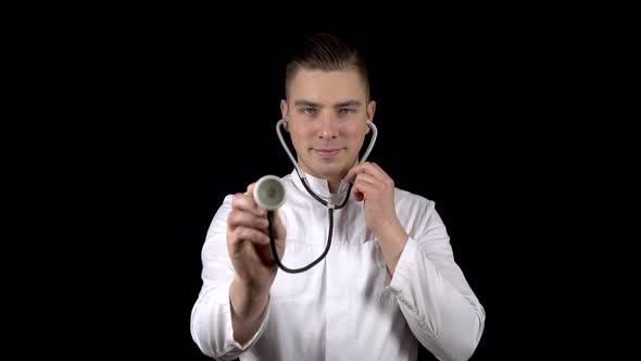 A Young Man Doctor Stands with with a Stethoscope and Listens on a Black Background. The Man