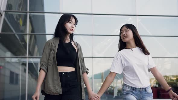 Asian Girls in Casual Youth Clothes Walking Together Holding by Hands and Carrying Shopping Bags