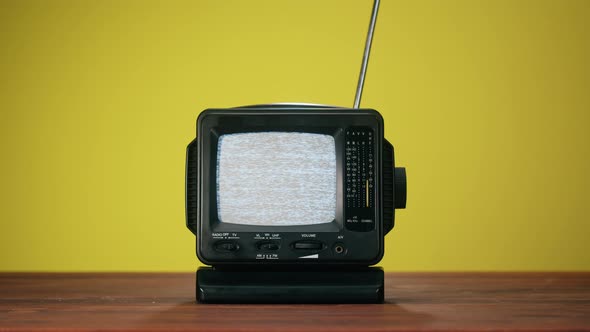 Turning on Small Old Television with Grey Interference Screen on Yellow Background