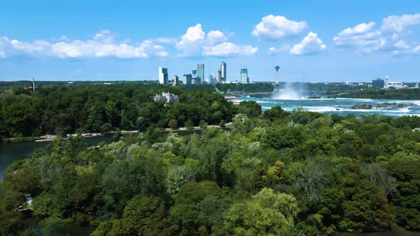 Aerial flight showing splashing niagra waterfalls, river and beautiful skyline in background during