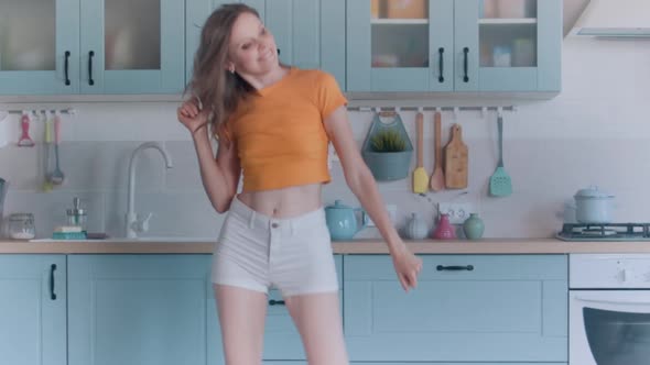 A Beautiful Woman in White Shorts is Relaxing at Home Dancing in the Kitchen