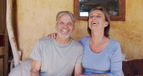 Portrait of smiling senior caucasian couple embracing and sitting on porch outside rustic house