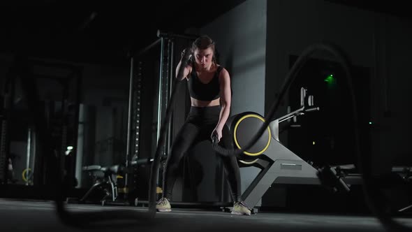 Caucasian Athletic Female Performs Exercises with Battle Ropes Endurance Training in the Gym Slow