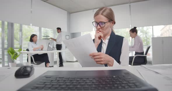 Focused Businesswoman Reading Documents Sitting at Desk in Office