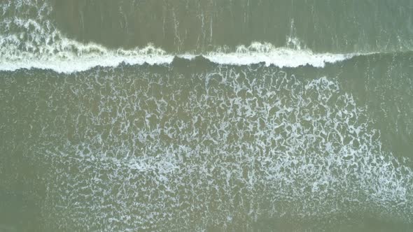 Aerial Vertical View at Large Waves Crashing Against a Beach on Cloudy Day