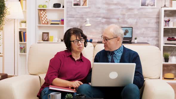 Elderly Couple Sitting on Sofa Using Laptop for Online Shopping