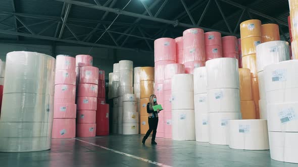 Female Factory Worker Observing a Warehouse Full of Big Paper Rolls