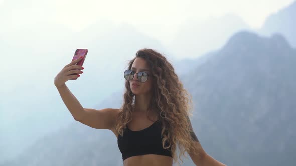 Woman with Long Curly Hair Makes Selfie Against Mountains