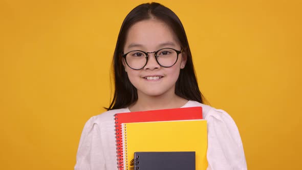 Cute Girl in Glasses and Holding Textbooks Smiling at Camera Orange Studio Background