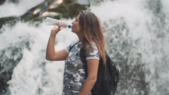 Attractive Girl Drinks Cold Water From a Bottle and Quenches Thirst While Standing on a Stone Near a