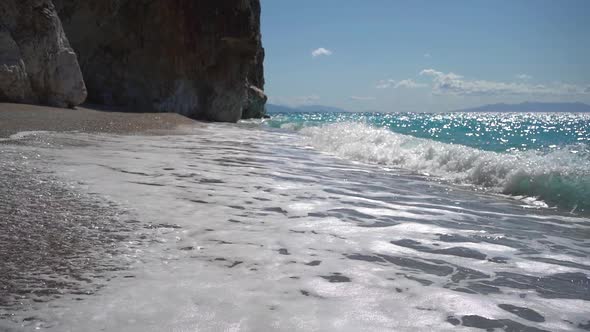 Long Sea Waves with Foam on the Beach Near the Huge Rock at Sunny Day