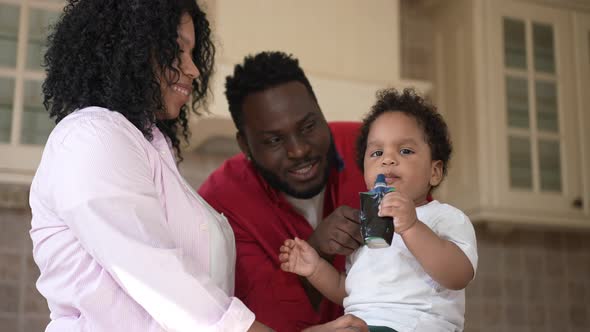 Cute Little African American Boy Eating Children Food From Tube with Couple of Smiling Loving