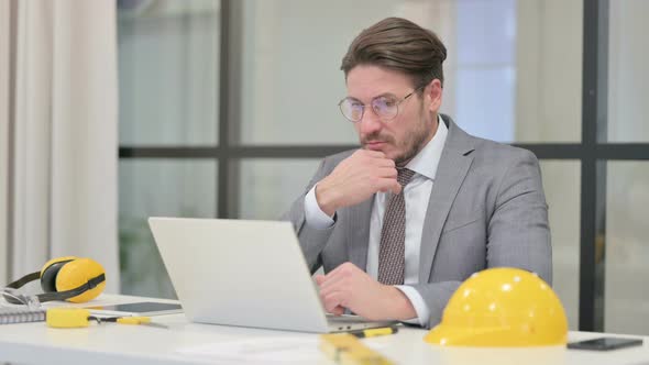 Middle Aged Engineer Thinking while Working on Laptop in Office