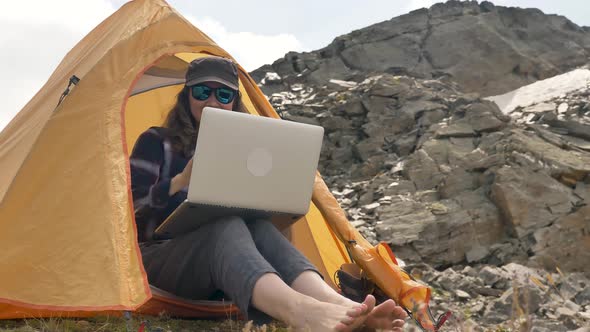 Lady Sits on Hill Top and Types on Laptop Against Mountains