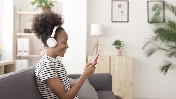 Young African American Woman Using Smartphone While Relaxing in Living Room