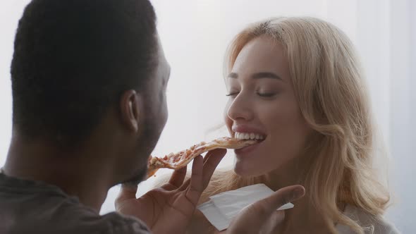 Diverse Couple Eating Pizza Feeding Each Other Flirting Indoors