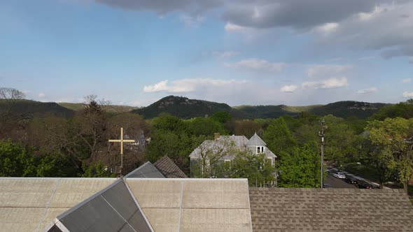 Aerial view starting at a church building roof with cross and skylights looking toward bluffs.