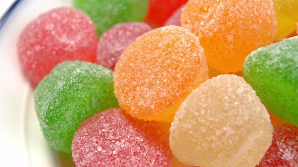 Assorted sugary marmalade candies on white plate. Translucent candied jelly round shape. Macro