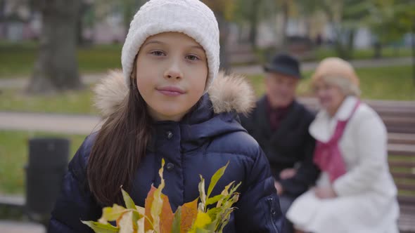 Smiling Caucasian Girl in White Hat Holding a Bunch of Yellow Leaves and Looking at the Camera