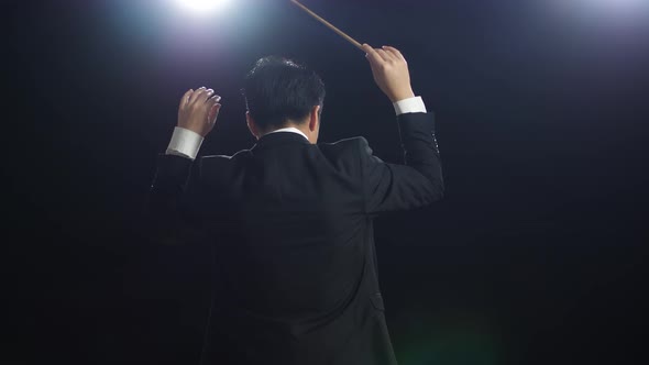 Back View Of Asian Conductor Man Holding A Baton And Showing Gesture In The Black Studio