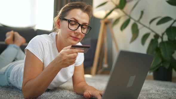 Woman with Glasses is Lies on the Floor and Makes an Online Purchase Using a Credit Card and