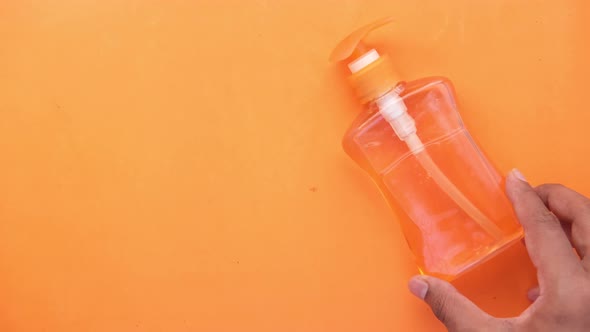 Putting Hand Wash Liquid Container and Face Mask on Orange Background