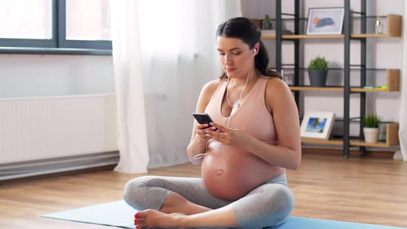 Pregnant Woman with Earphones Doing Yoga at Home