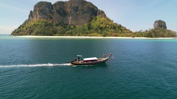 aerial drone parallel with a tourist at the front of a thai longtail boat motoring through the blue