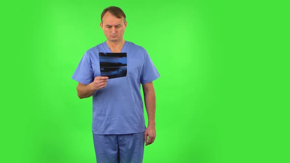 Male Doctor in Blue Coat Reviewing X-ray Pointing on Snapshot. Green Screen
