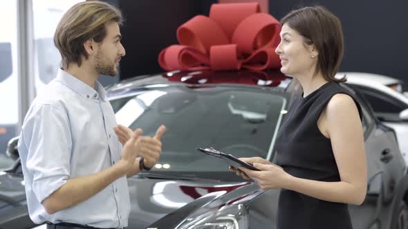 Cheerful Wealthy Man Talking with Car Dealer in Showroom, Side View of Positive Caucasian Buyer