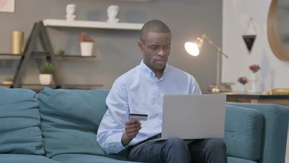 African Man Making Online Payment Failure on Laptop on Sofa