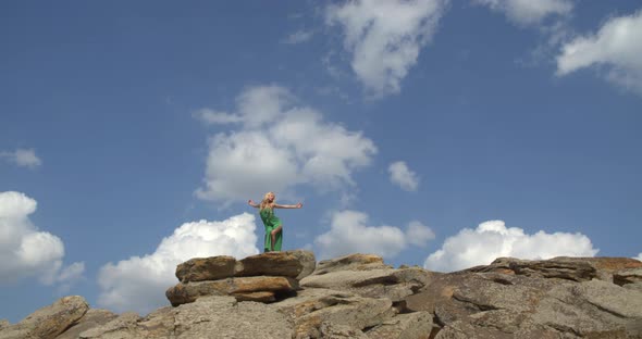 Blonde Woman in Green Dress is Dancing on the Hill Covered in Rocks