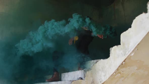 Mixed race man holding green flare sitting on stairs in an empty building