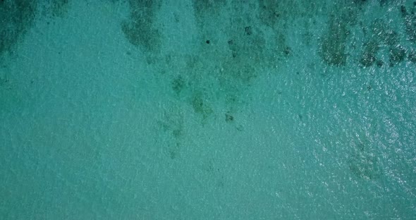 Wide fly over island view of a white sandy paradise beach and aqua blue ocean background in vibrant 