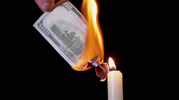 Burning 100 Dollar Bill Over a Candle Flame on a Black Background