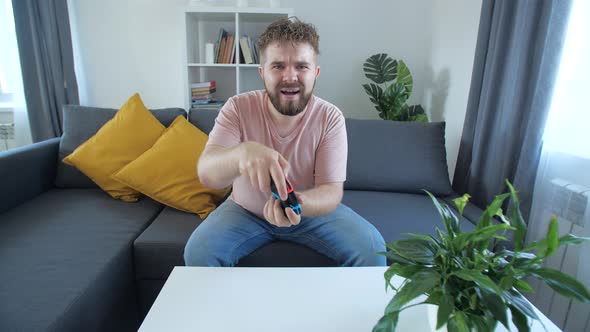 Attractive Man with Bristle and Toothy Grin Holding Joystick and Playing Videogames on Tv Sits at