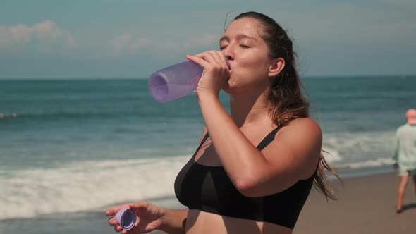 Attractive Lady Drinking Water After Jogging Along Sandy Seashore