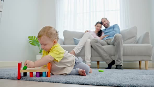 Caucasian happy loving parents look at baby toddler son play on floor in living room in house.