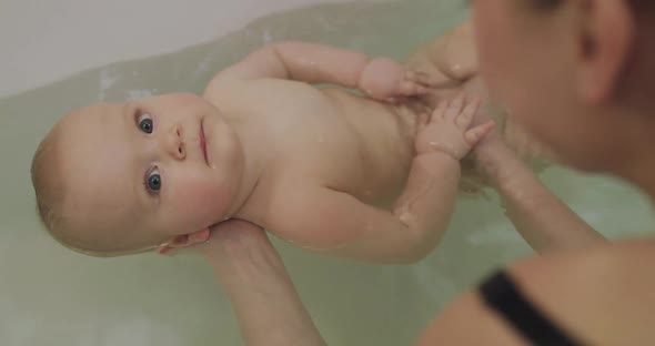 Cute Bare Baby Looking Up with His Blue Eyes During Bathing in Tub
