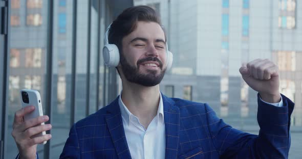 Caucasian Happy Beautiful Man in Suit in Headphones Dansing on Street and Listening to Music