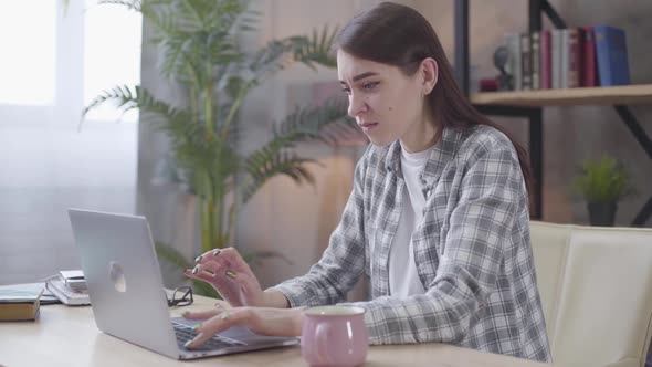 Portrait of Angry Caucasian Girl Typing on Laptop Keyboard. Irritated Female Freelancer Arguing