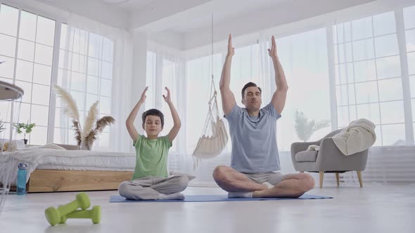 Man with Son Doing Yoga Sitting on Mat at Home