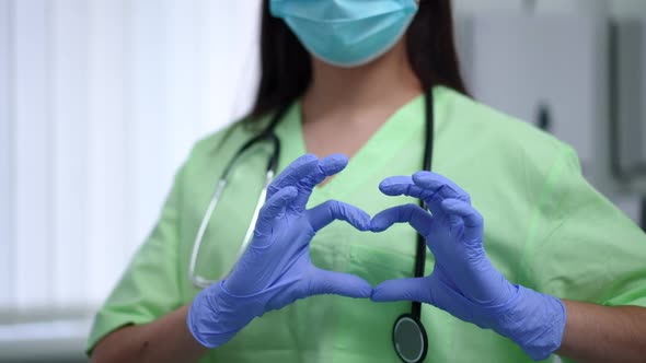 Unrecognizable Female Doctor Gesturing Heart Shape at Chest Standing in Hospital Indoors